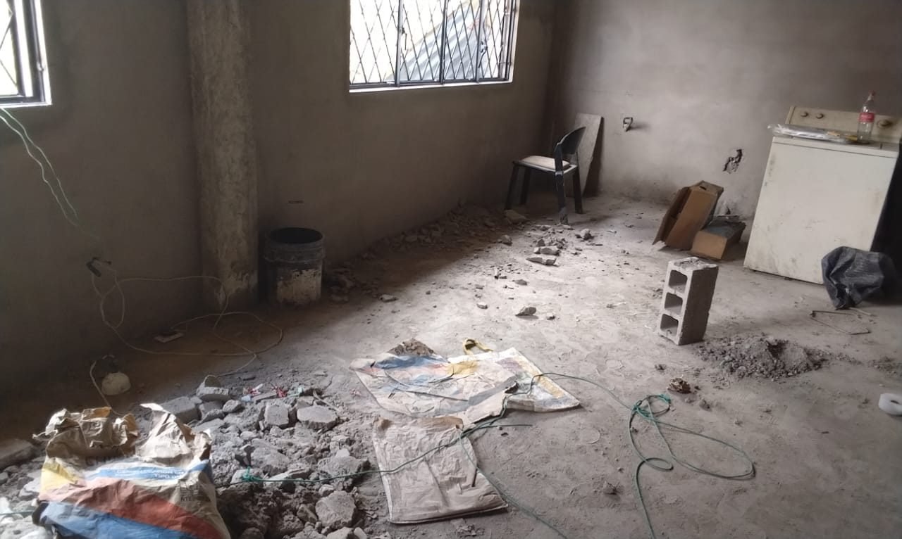 Interior del cuarto de oración en construcción: paredes enlucidas, ventanas instaladas con rejas, cables eléctricos a la vista y escombros en el piso.